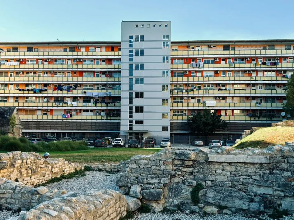 A tall modern building sitting behing a Roman stone wall